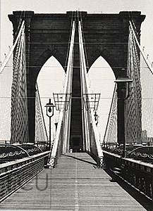 Black and white photo of the landmark Brooklyn Bridge and its stone arches and cables taken from the walkway in New York, New York