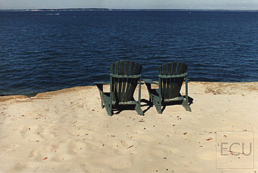 Color photo of chairs sitting atop of a beach escarpment overlooking Peconic Bay in Southampton, New York