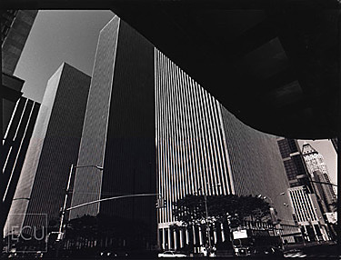 Black and white photo of the skyscrapers in midtown along Sixth Avenue taken from beneath the portico of the Radio City Music Hall